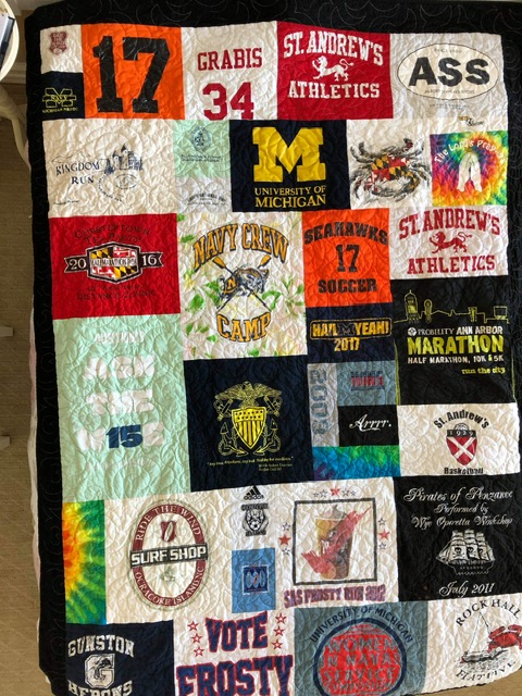 Finished memory quilt featuring sports team logos, university crests, marathon shirts, and travel souvenirs stitched into a single heirloom quilt.